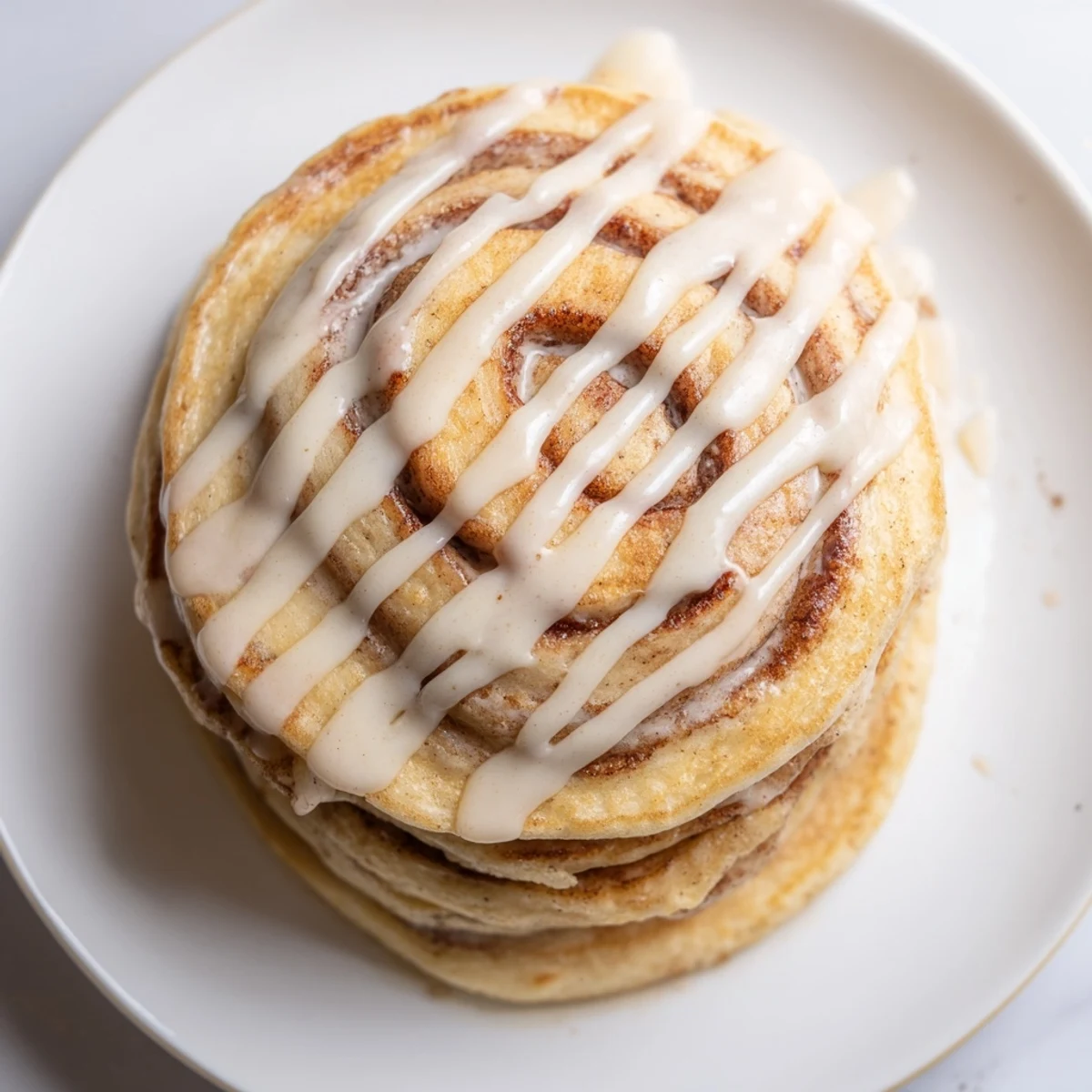 Fluffy Cinnamon Roll Pancakes drizzled with sweet cream cheese frosting, a perfect breakfast treat.