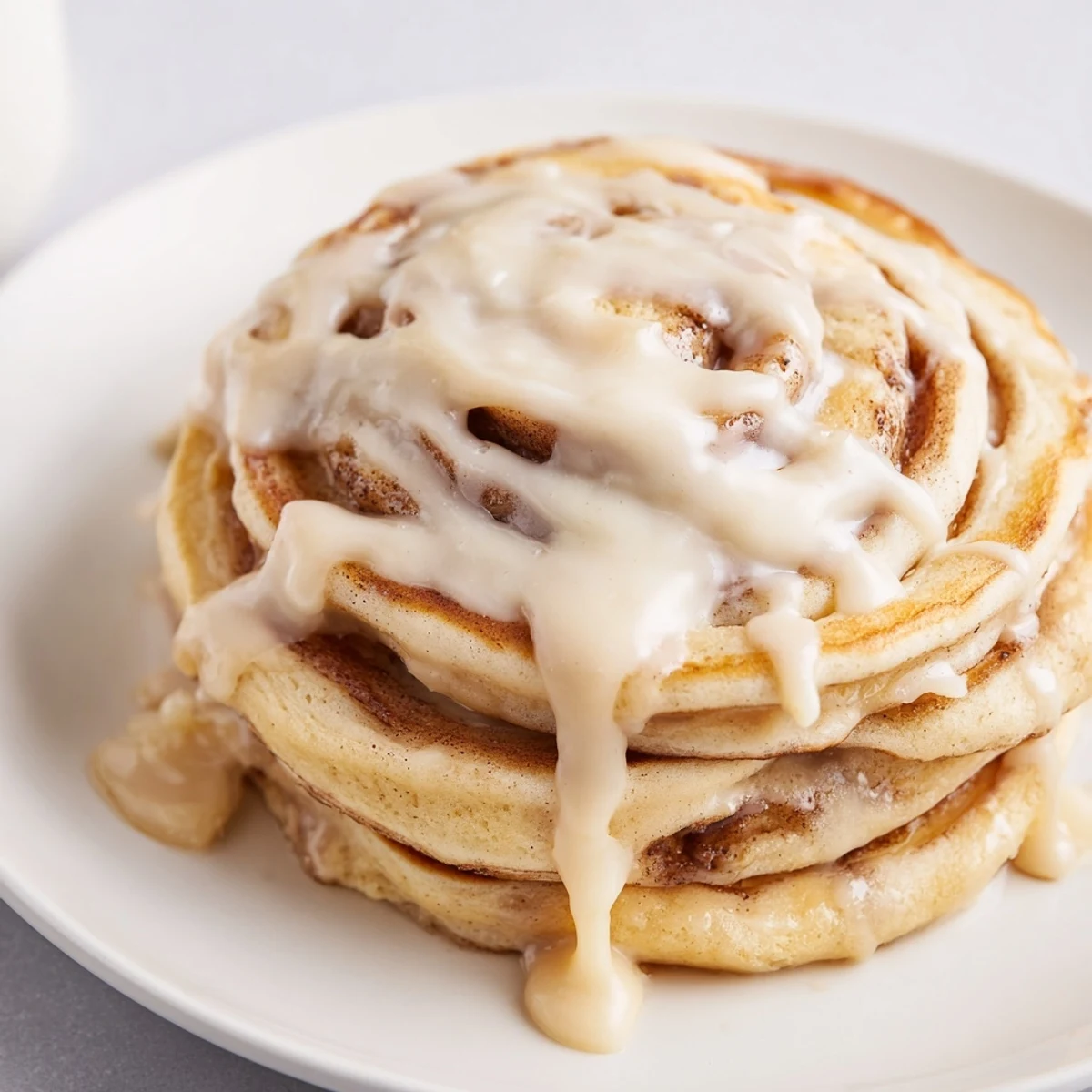 Close-up of freshly cooked Cinnamon Roll Pancakes, showing gooey cinnamon and creamy glaze dripping.