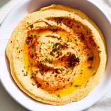 Smooth, homemade Roasted Red Pepper Hummus, drizzled with olive oil, ready to serve with pita.