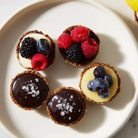 Sweet trio of mini dessert bites: creamy cheesecakes and chocolate tarts, glistening with toppings, ready.