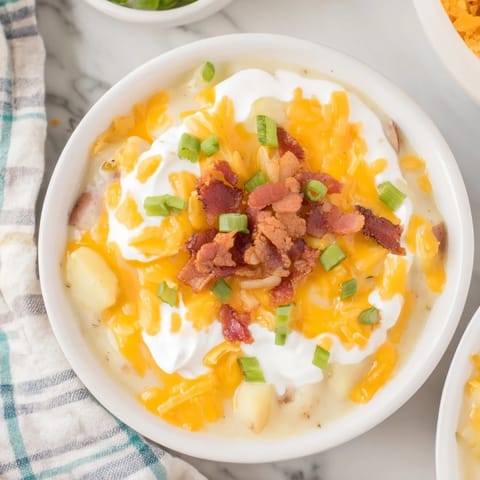 A steaming bowl of Crockpot Loaded Baked Potato Soup, garnished with green onions and crispy bacon bits.