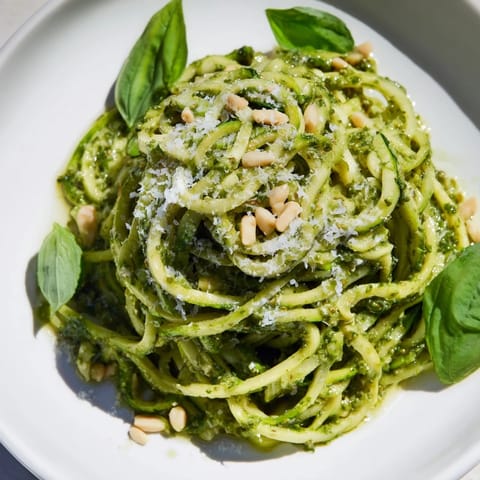 Bright green zucchini noodles with pesto garnished with fresh basil and Parmesan.  