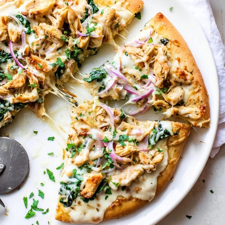 Close-up of Chicken Alfredo Pizza: creamy, cheesy swirl with chicken, ready to slice.