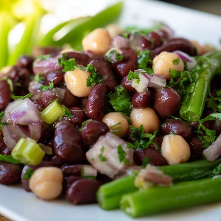 Close-up of chilled Three-Bean Salad featuring crisp celery and red onion chunks tossed in apple cider vinegar dressing, ready for a summer picnic.  