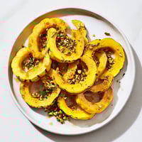 Golden baked delicata squash rings, drizzled with maple syrup and sprinkled with pistachios.